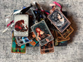 Load image into Gallery viewer, stack of tarot card ornaments in various colors with various characters. 
