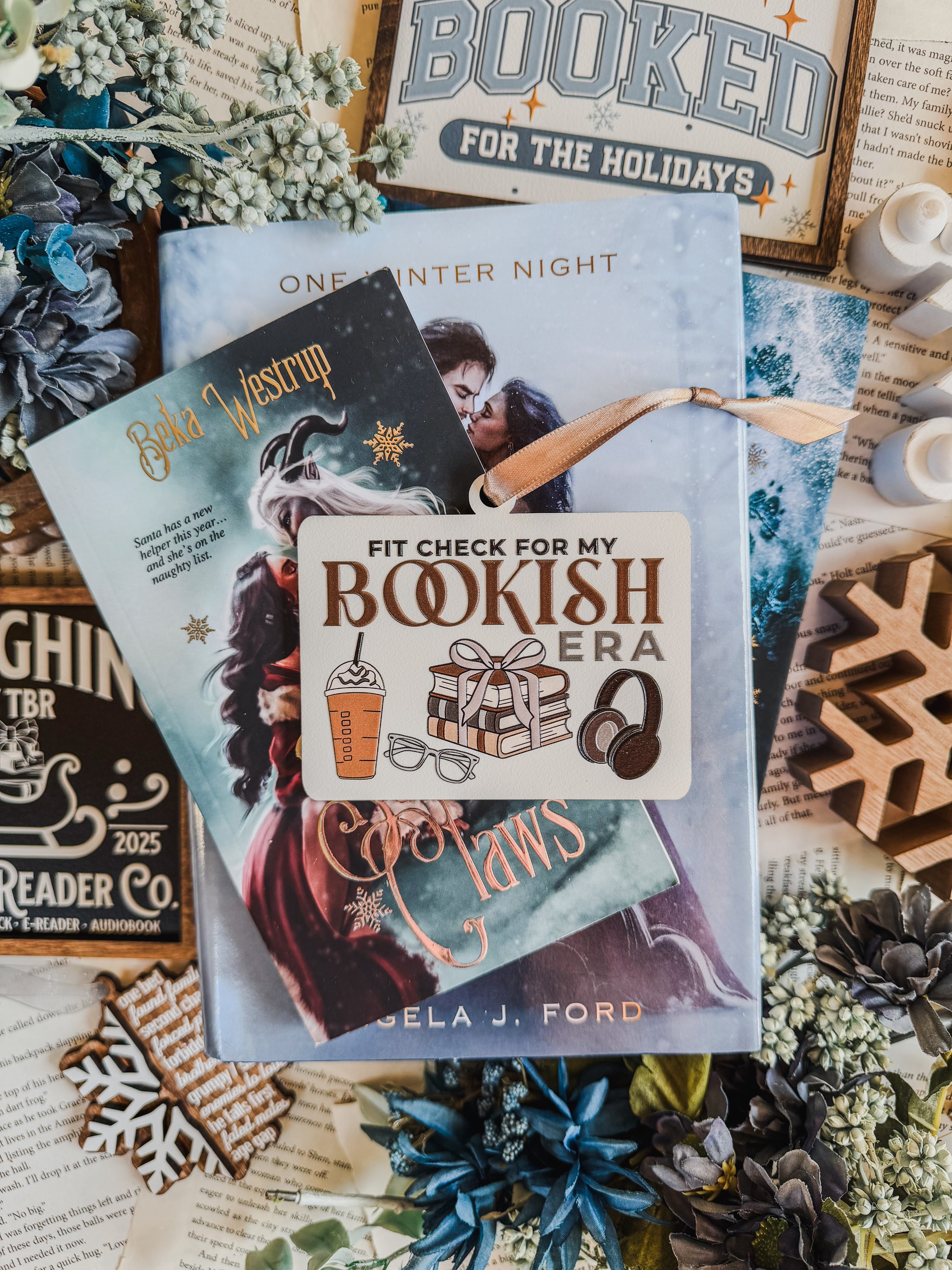 Wooden ornament with a white background and tan ribbon. Text reads "Fit Check For My Bookish Era" with surrounding graphics of a latte, glasses, a stack of books, and headphones. © FireDrake Artistry