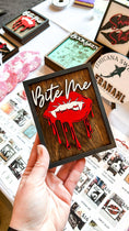Load image into Gallery viewer, Bite Me Shelf Sign - firedrakeartistry wooden sign with natural background, dark grey frams, white "Bite Me" wording and red vampire lips.
