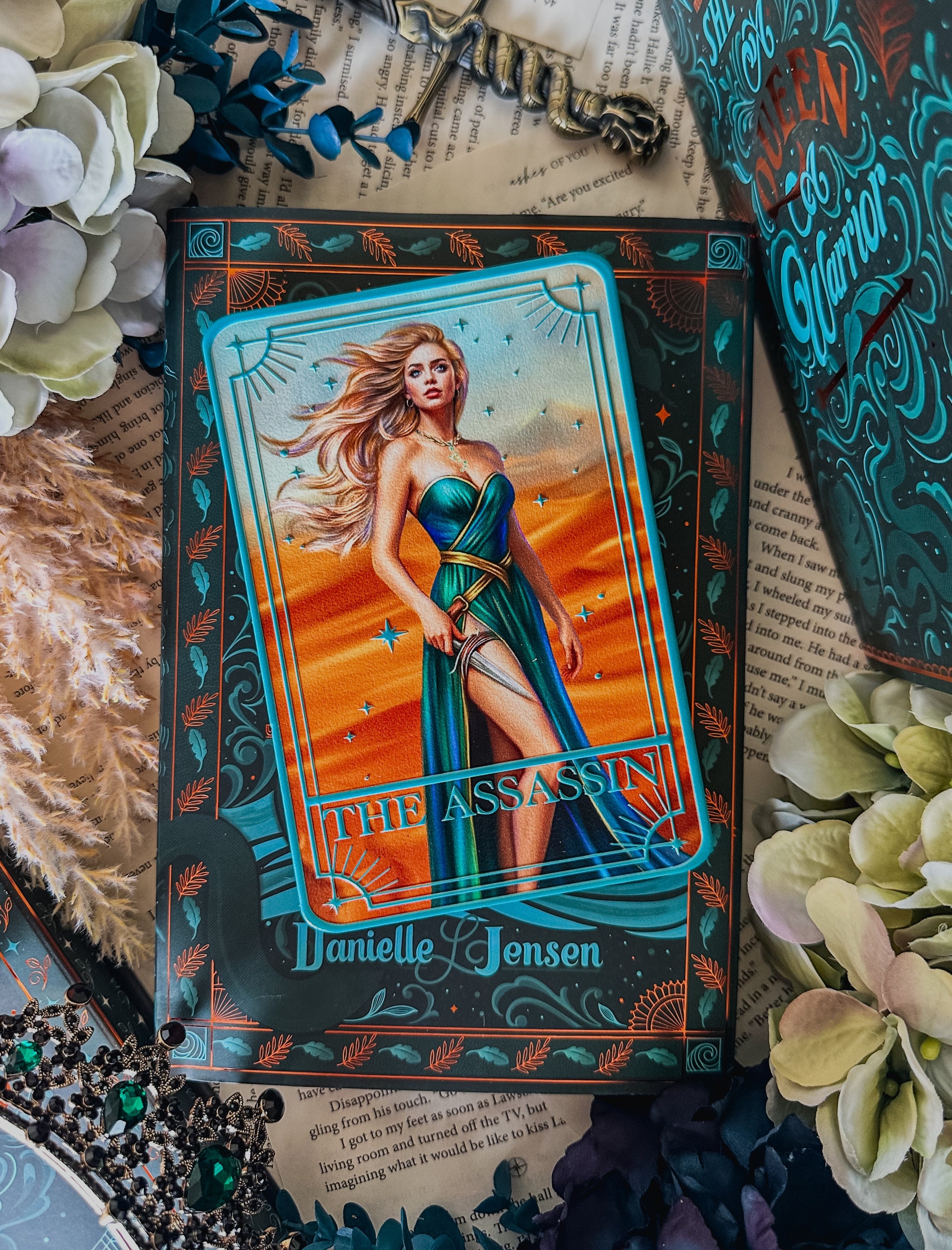 Tarot card featuring a woman labeled 'The Assassin' by Danielle Jensen, surrounded by decorative elements.