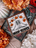 Load image into Gallery viewer, Mood Reader Sign. A square decorative sign made of wood with a wood-stained frame. UV printed skeleton in a zen position, surrounded by pumpkins with multiple faces, with the text 'MOOD READER' across the center. FireDrake Artistry 2025
