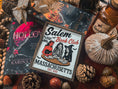 Load image into Gallery viewer, Salem Book Club Sign. White shelf sign with a wood grain border featuring a devil, witch, and skeleton women at a table reading. Top reads “SALEM BOOK CLUB” and the bottom reads “MASSACHUSETTS EST 1692” ©️Fire Drake Artistry 2025
