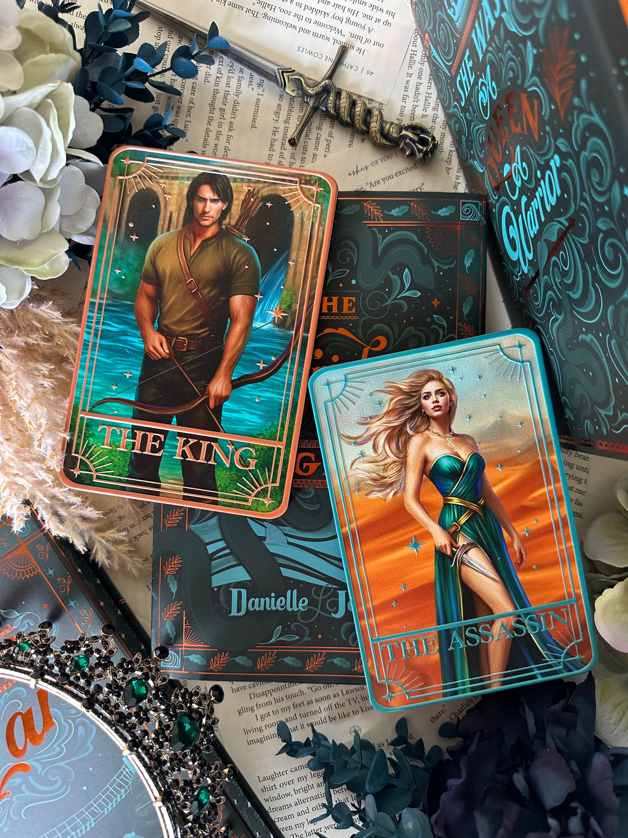 Two tarot cards, 'The King' and 'The Queen', on a surface with decorative elements of books and flowers. 