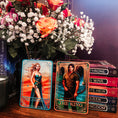 Load image into Gallery viewer, Two tarot cards titled 'The Assassin' and 'The King' with a bouquet of flowers and books in the background.
