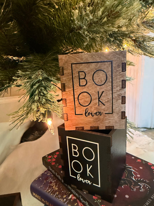 Wooden and black boxes with "Book Lover" printed on them. Bookstack and Christmas tree in the background. 