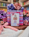 Load image into Gallery viewer, Tarot card title “The Reader” with a girl reading an open book in front of a bookstack with flowers and other decorative items in the background. 
