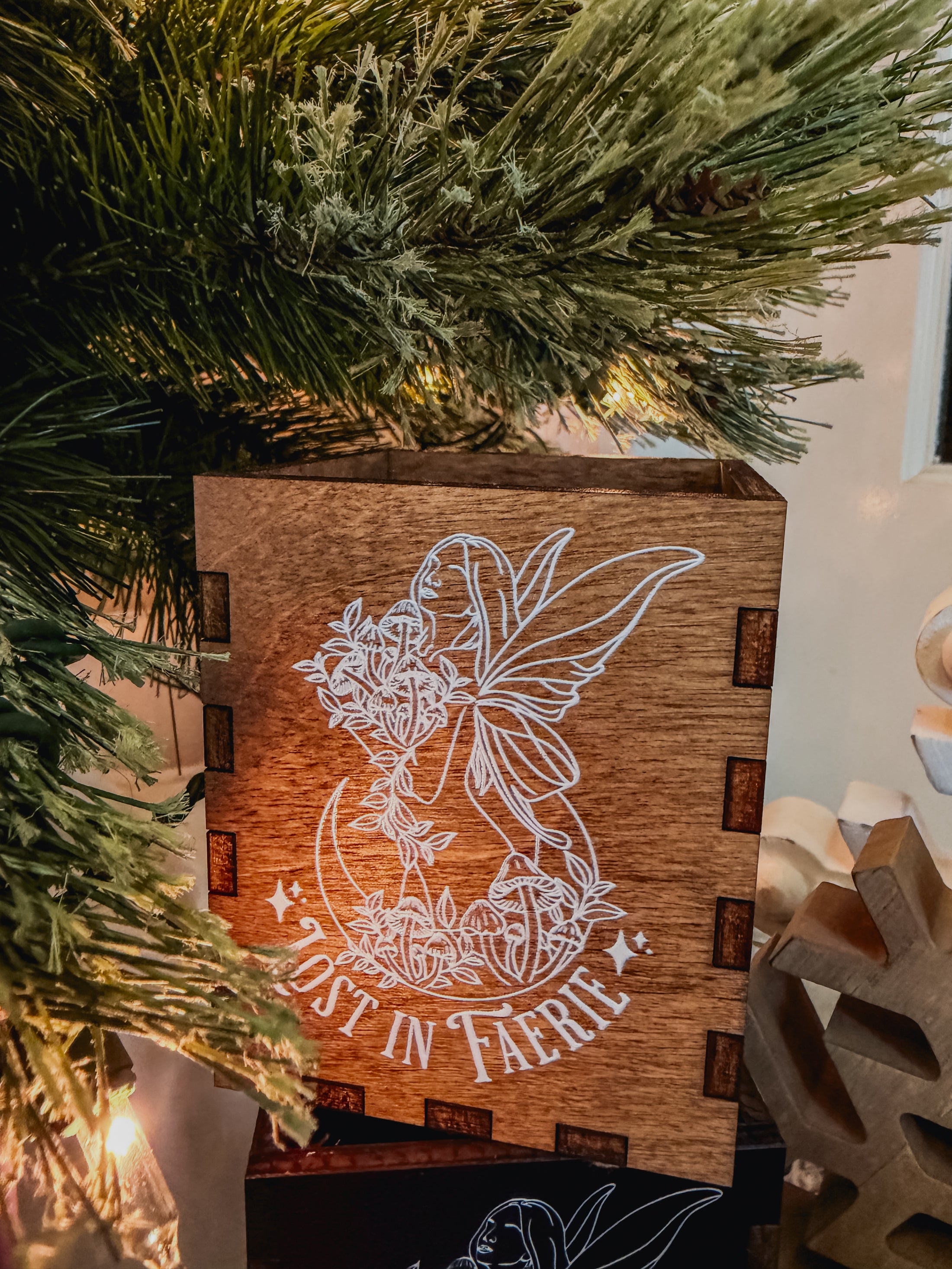 Wooden  box with printed fairy design and 'Lost in Faerie' text, against a Christmas tree background.
