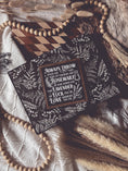 Load image into Gallery viewer, Black shelf sign with white text surrounded by a dark wood border. Graphics of a vial, lavender, rosemary and stars surround text that reads: “Always throw salt over your left shoulder. Keep rosemary by your garden gate. Plant lavender for luck. Fall in love whenever you can.” 
