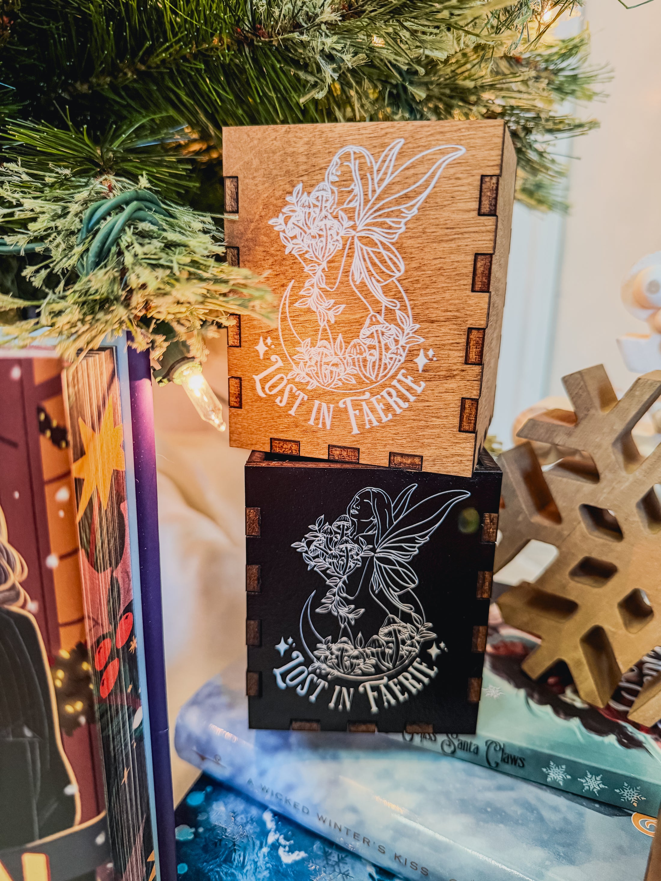 Wooden and black boxes with printed fairy design and 'Lost in Faerie' text, against a Christmas tree background.