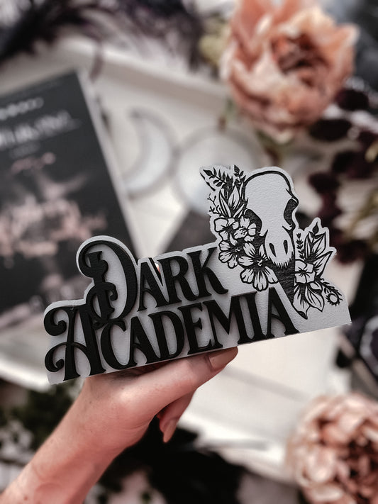 Dark Academia Sign. Grey wooden block sign with 3D text that reads "DARK ACADEMIA" beside a skull and flowers. 