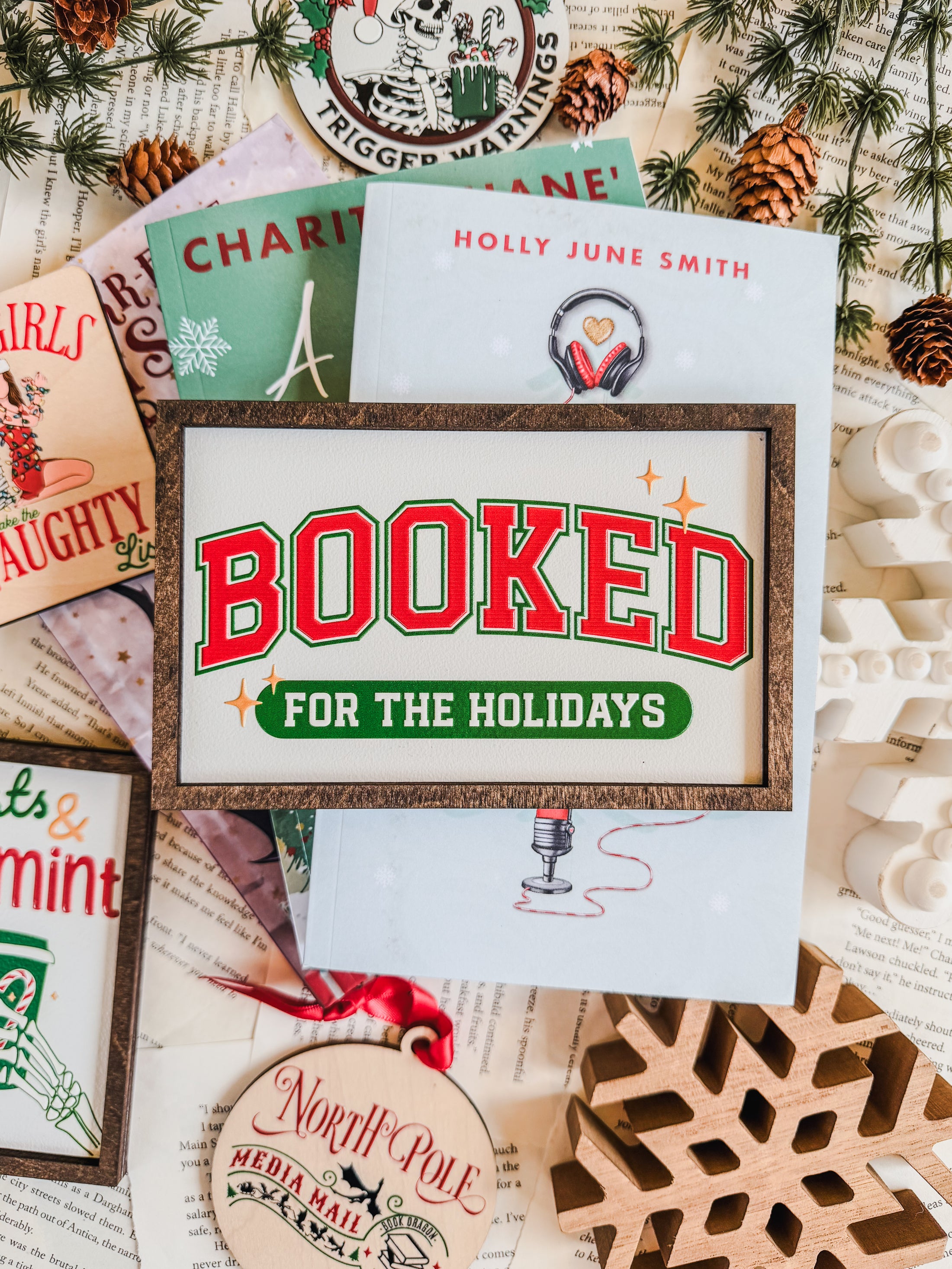Decorative sign with a wooden frame that reads 'Booked for the Holidays' in red on a white background. © FireDrake Artistry 2025.