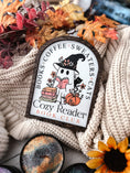 Load image into Gallery viewer, Cozy Reader Ghosty Sign. White background with a wood border with a colorful UV printed design. 
Featuring a ghost reading a book and wearing a witch hat, surrounded by flowers and a pumpkin. Text above reads “Books. Coffee. Sweaters. Cats.” While the text below reads “Cozy Reader Book Club.” 
