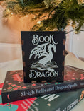 Load image into Gallery viewer, Black Wooden box with 'Book Dragon' design on top of books with a Christmas tree in the background
