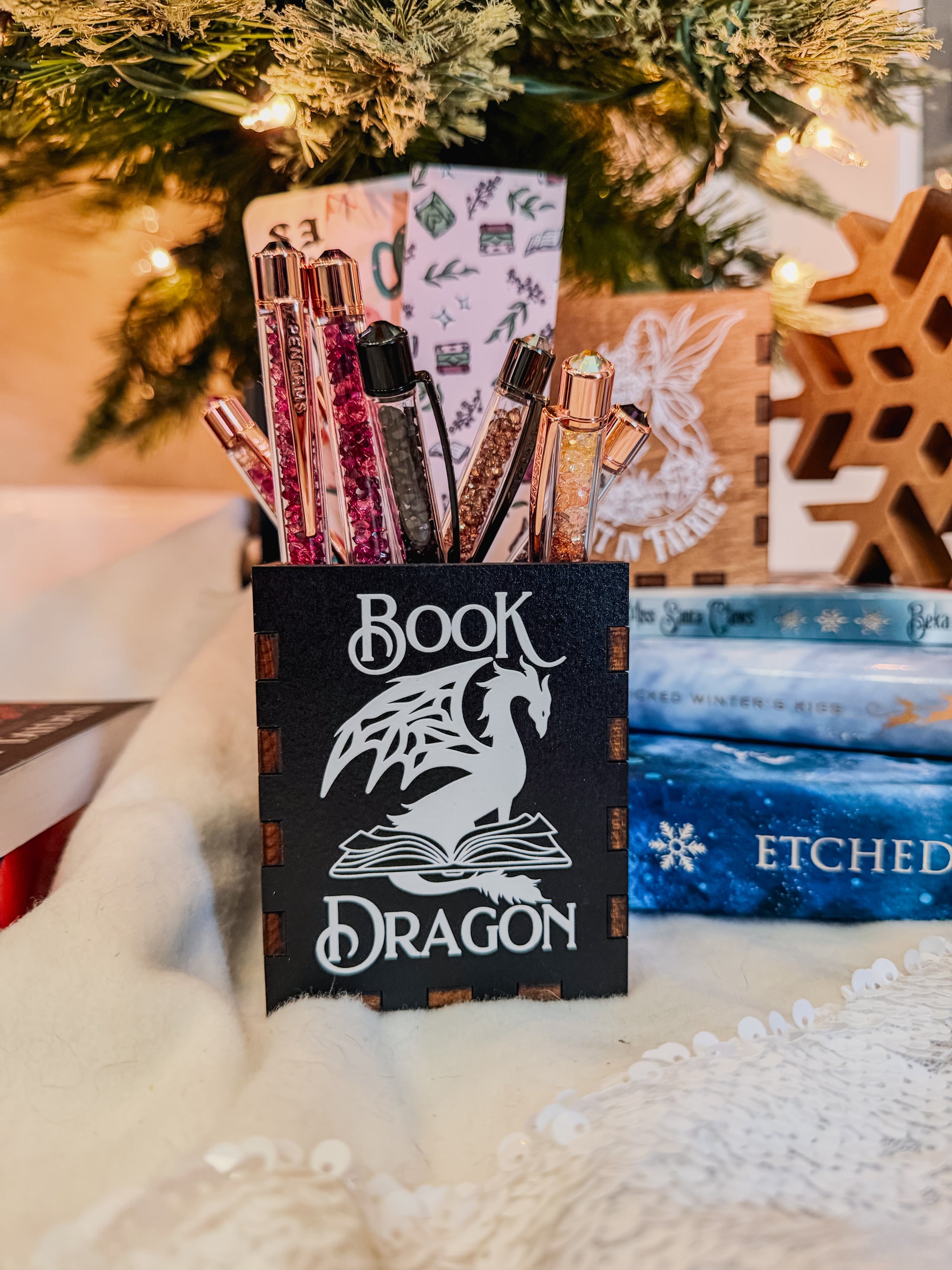 Wooden box with 'Book Dragon' design on top of books with a Christmas tree in the background