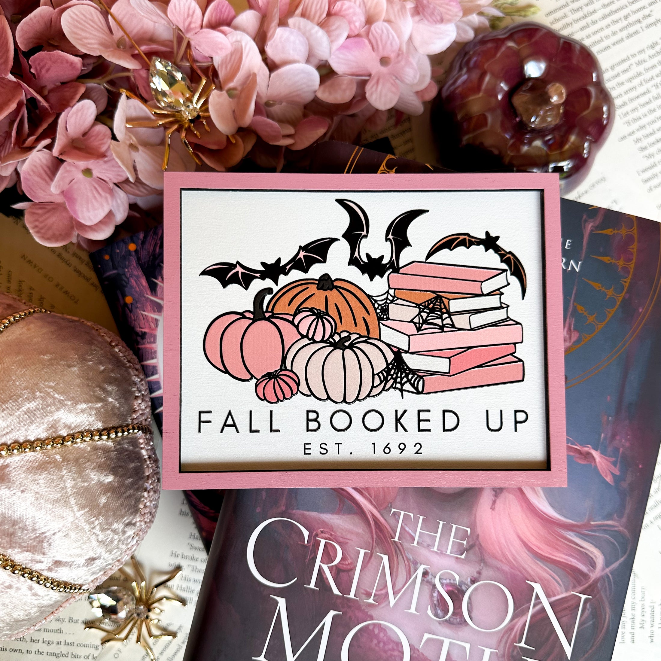 Fall Booked Up Sign - Pink Version- ©️ Fire Drake Artistry 2025. Wooden sign with white background and pink frame, UV printed design with a cluster of pumpkins beside a stack of pink books and bats flying around. 