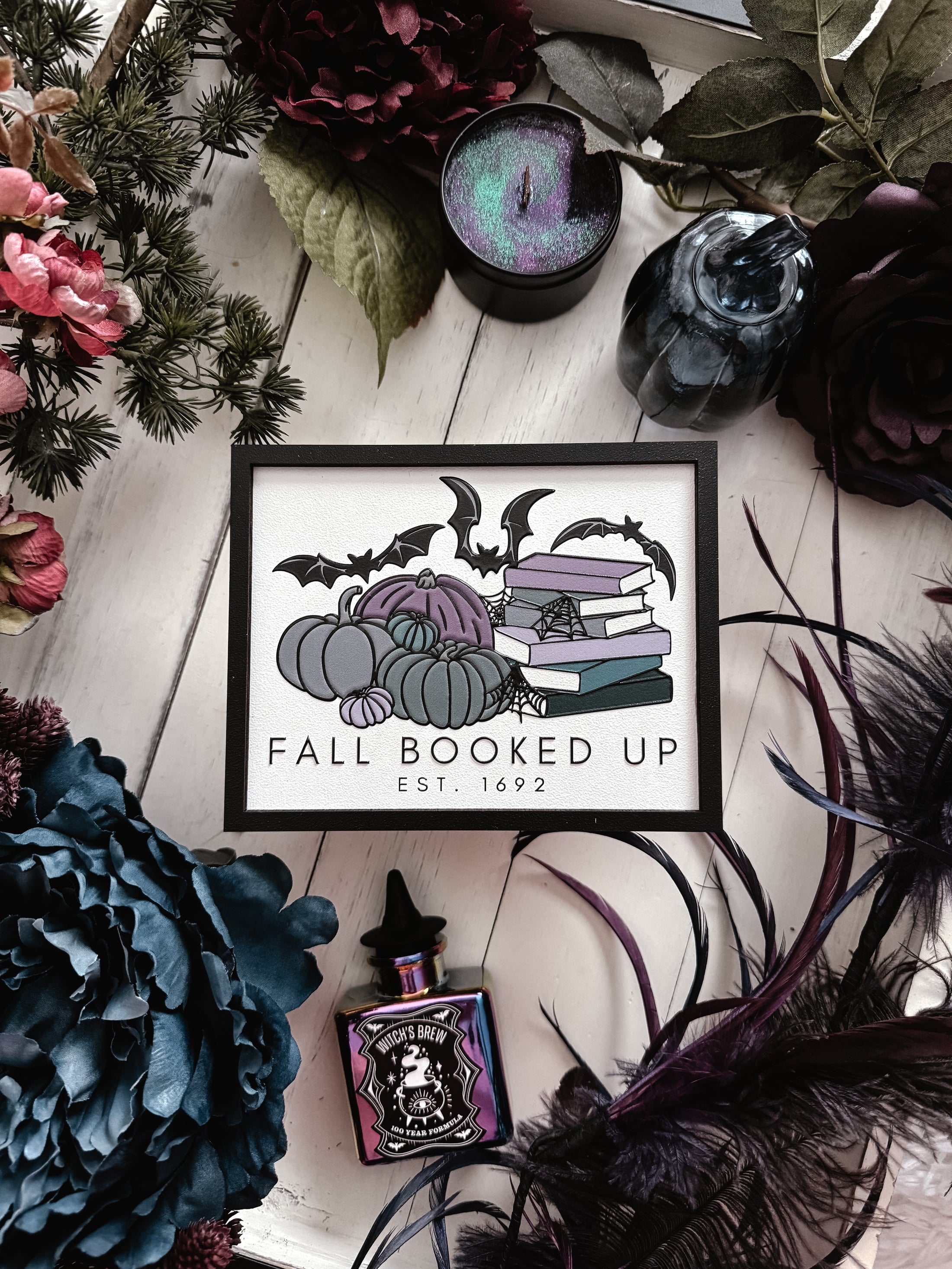 Fall Booked Up Sign - Purple Version- ©️ Fire Drake Artistry 2025. Wooden sign with white background and black frame, UV printed design with a cluster of pumpkins beside a stack of books and bats flying around. 