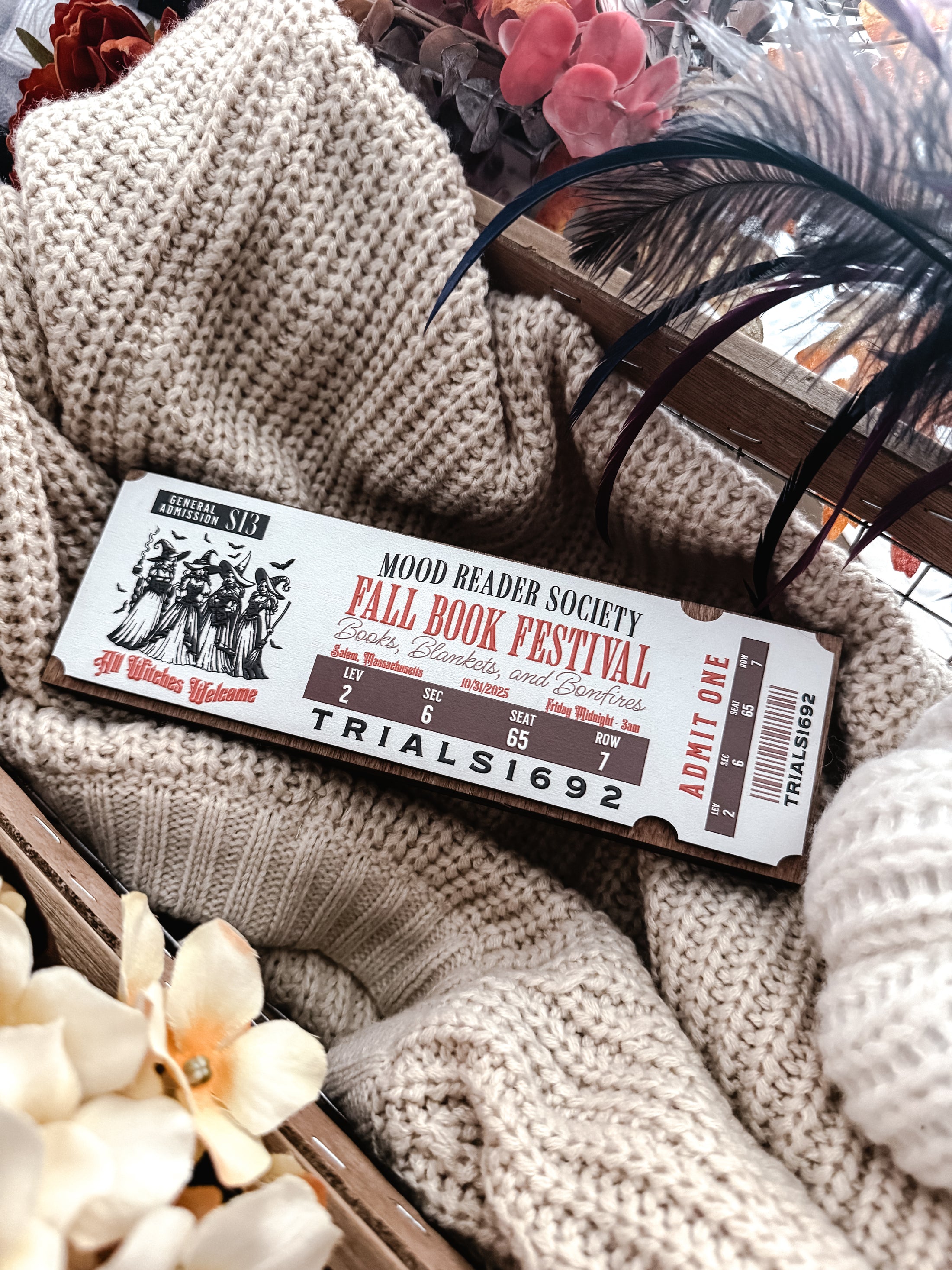 Fall Book Festival Ticket Sign. Thick Wooden sign with a white background shaped like a ticket. Orange text that reads “Fall Book Festival” with a date and ticket details. Featuring an image of witches, which beneath reads “witches welcome”. ©️FireDrake Artistry 2025