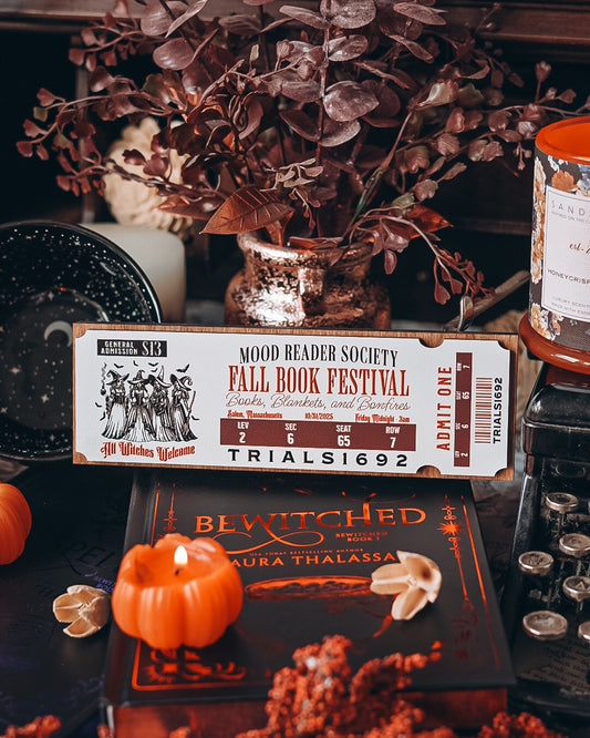 Fall Book Festival Ticket Sign. Thick Wooden sign with a white background shaped like a ticket. Orange text that reads “Fall Book Festival” with a date and ticket details. Featuring an image of witches, which beneath reads “witches welcome”. ©️FireDrake Artistry 2025