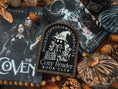Load image into Gallery viewer, Cozy Reader Ghosty Sign. Black background with a dark wood border with a white design engraved. 
Featuring a ghost reading a book and wearing a witch hat, surrounded by flowers and a pumpkin. Text above reads “Books. Coffee. Sweaters. Cats.” While the text below reads “Cozy Reader Book Club.” 
