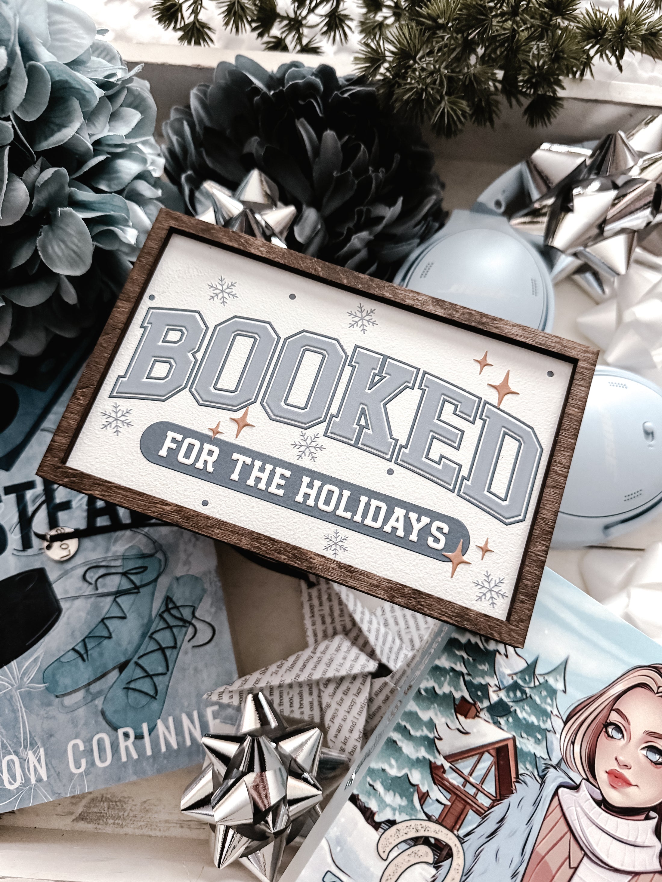 Decorative sign with a wooden frame that reads 'Booked for the Holidays' in blue on a white background. © FireDrake Artistry 2025.
