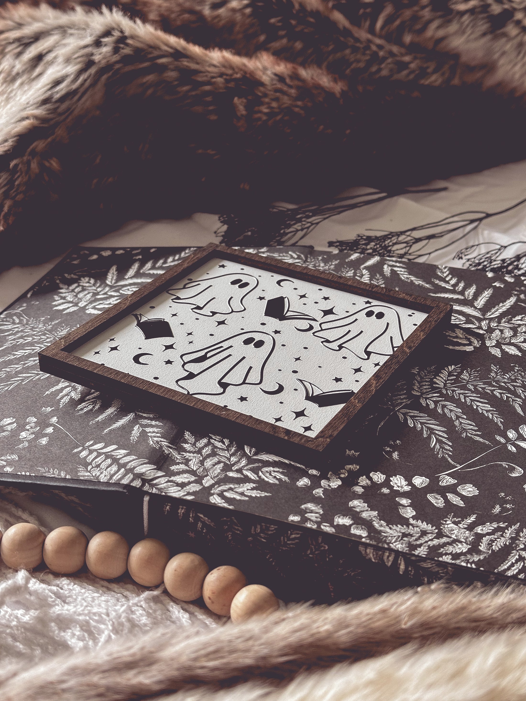 Boo Books Shelf Sign. A white. wooden square sign with a wood frame featuring illustrations of ghosts, books and stars. 2023 FireDrake Artistry®