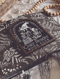 Load image into Gallery viewer, Cozy Reader Ghosty Sign. Black background with a dark wood border with a white design engraved. 
Featuring a ghost reading a book and wearing a witch hat, surrounded by flowers and a pumpkin. Text above reads “Books. Coffee. Sweaters. Cats.” While the text below reads “Cozy Reader Book Club.” 
