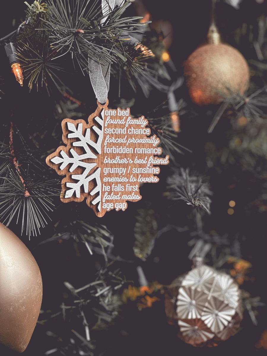 A wooden ornament in the shape of a snowflake featuring a list of tropes on the right side in the shape of a snowflake. © FireDrake Artistry 2025