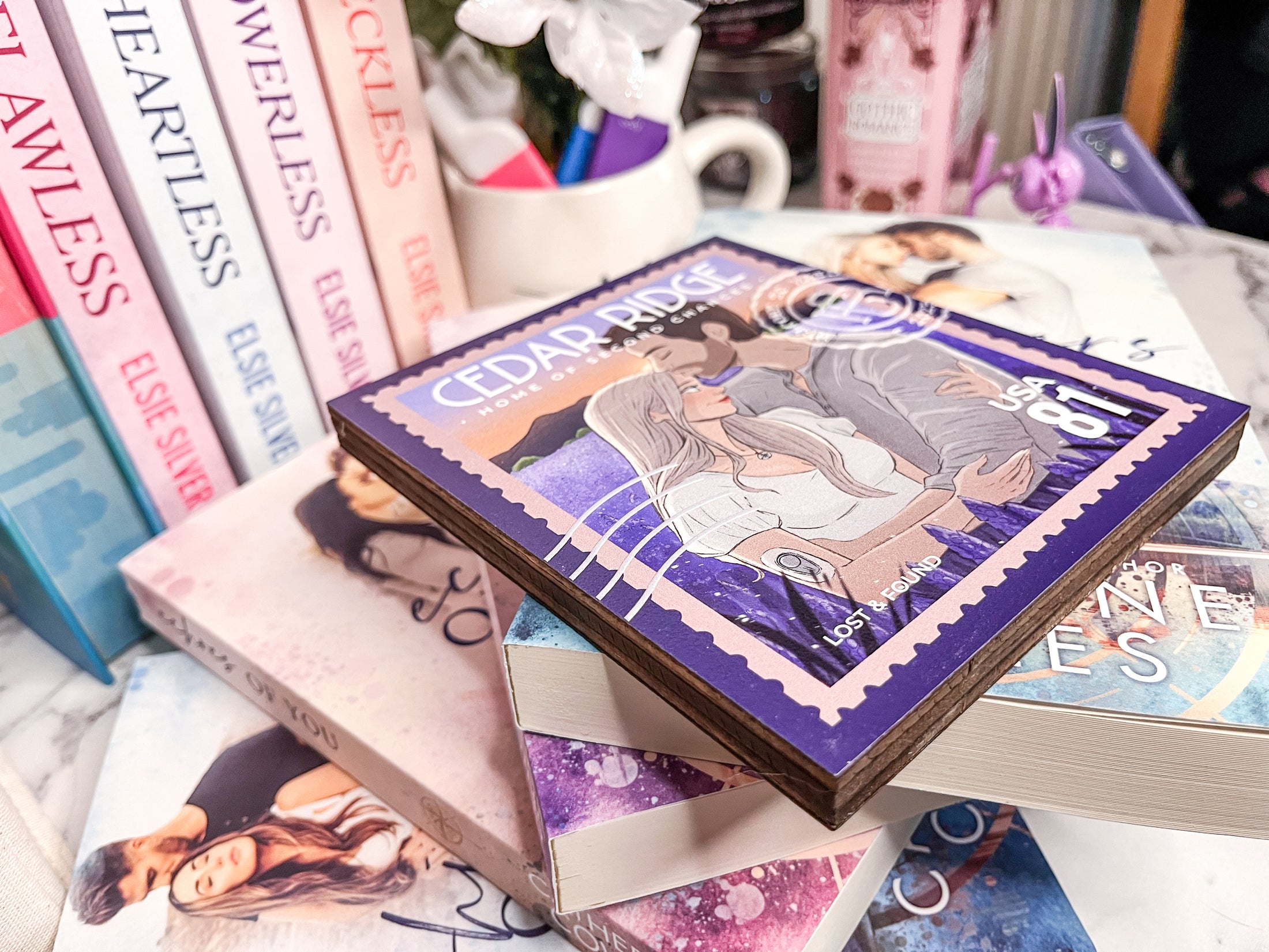 A postage stamp featuring artwork of a romantic scene, on top of a stack of books with a book stack and mug with flowers in the background. 