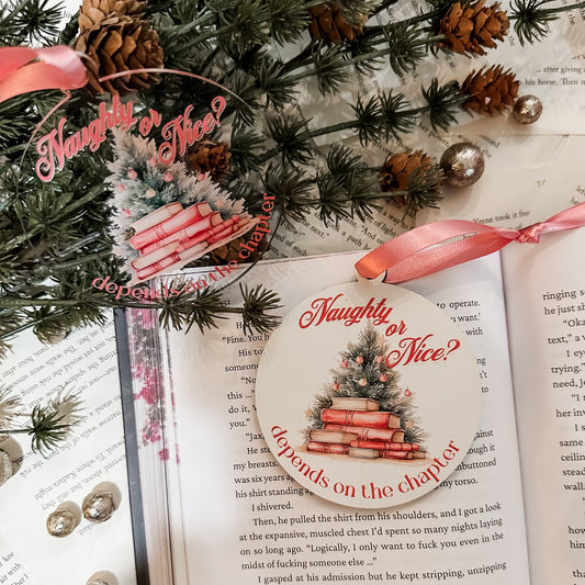 Wooden white and acrylic ornaments featuring pink text that reads "Naughty or Nice? Depends on the Chapter" surrounding a Christmas tree and books. ©FireDrake Artistry 2023 