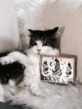 Load image into Gallery viewer, Indoor Cat Book Club Sign. White wooden sign with a wood frame. Design featuring a floral cat sitting atop a pile of books flanked by flowers, a moon, and some stars. Text below reads "Indoor Cat Book Club". Featuring a grey and white cat. 2023 FireDrake Artistry®

