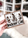 Load image into Gallery viewer, Indoor Cat Book Club Sign. White wooden sign with a wood frame. Design featuring a floral cat sitting atop a pile of books flanked by flowers, a moon, and some stars. Text below reads "Indoor Cat Book Club". 2023 FireDrake Artistry®
