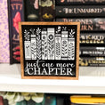 Load image into Gallery viewer, Just One More Chapter Shelf Sign. A wooden shelf sign with black and white artwork featuring book spines and the text 'just one more chapter'. 2024 Fire Drake Artistry.
