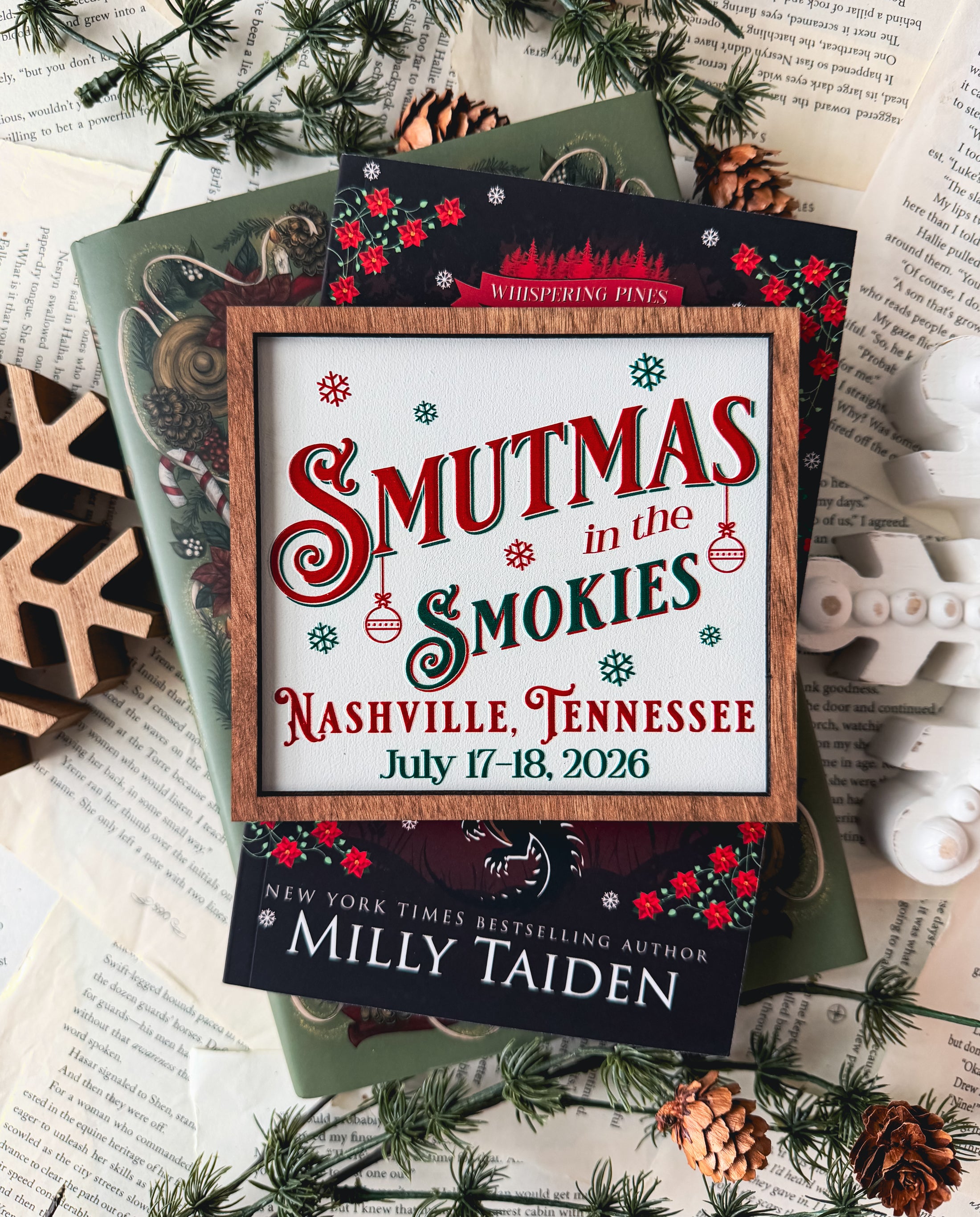 Woods sign with "Smutmas in the Smokies" and other event information printed on it, on top of red and green books. Book pages in the background with other holiday decor. 
