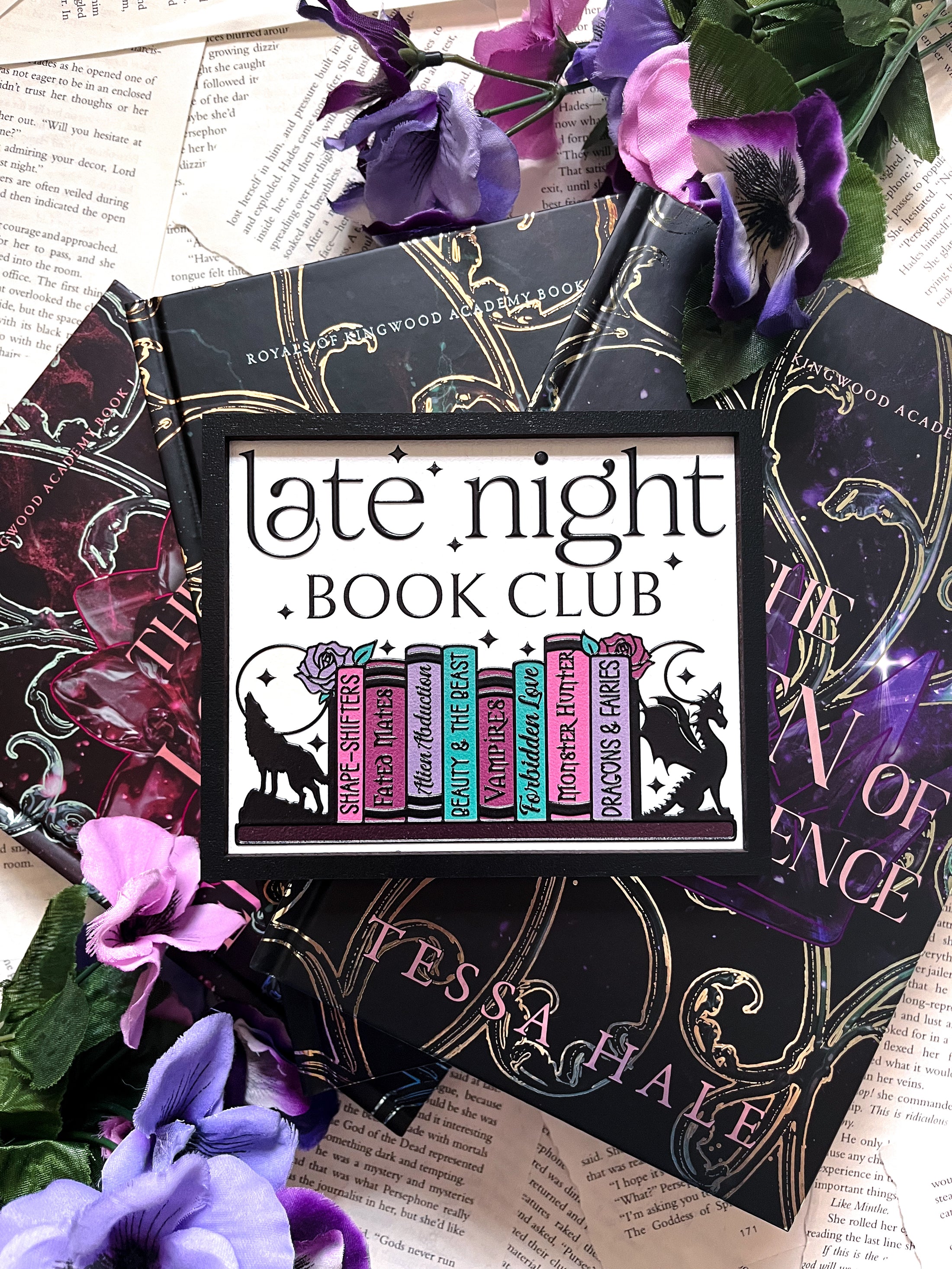 Late Night Book Club Sign. A white wooden shelf sign with a black border. UV printed design that reads "LATE NIGHT BOOK CLUB" above an assortment of books with a wolf and dragon bookends. 2024 FireDrake Artistry®